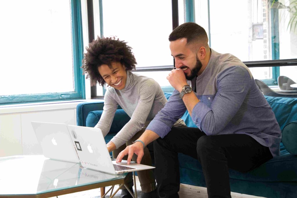 Two individuals working on laptops while seated on a couch.
